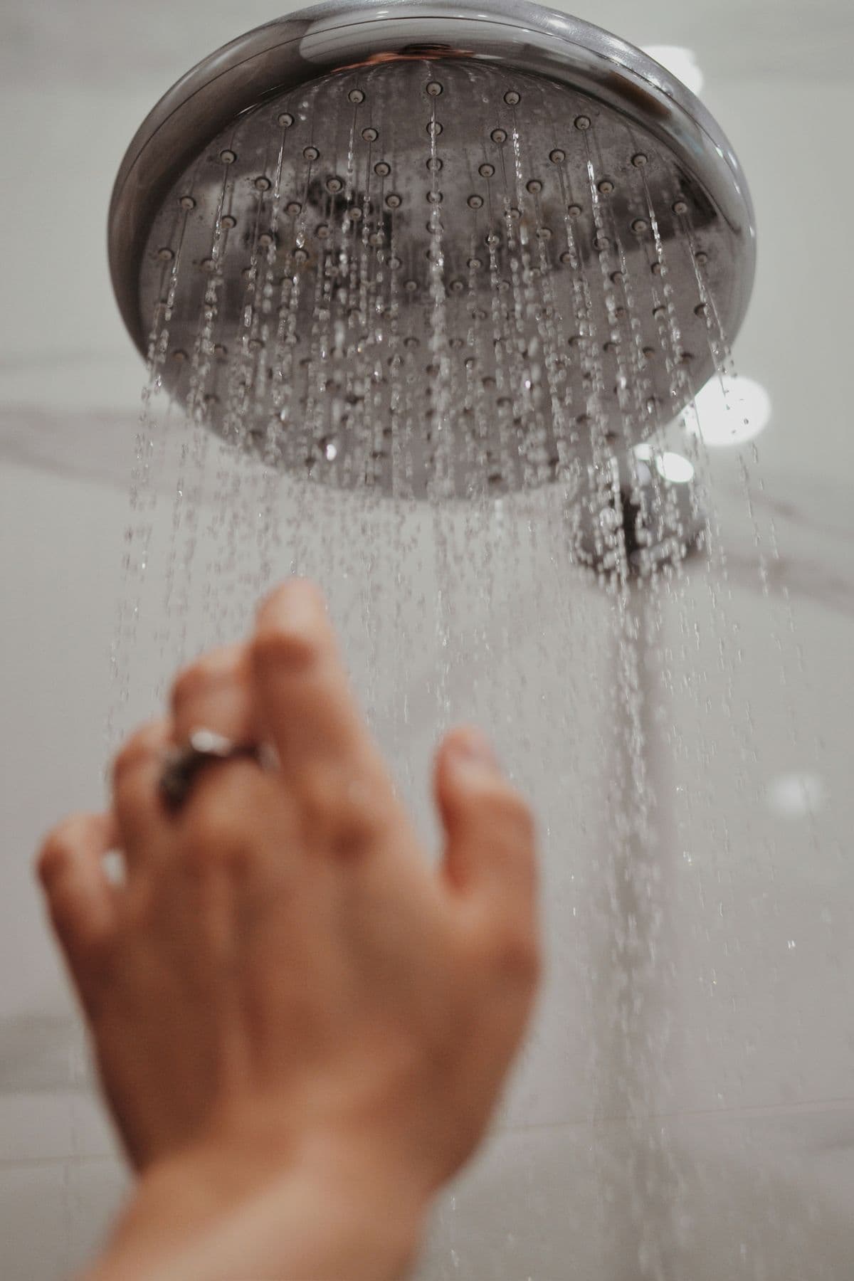 Wasser aus einem Duschkopf trifft auf eine ausgestreckte Hand.